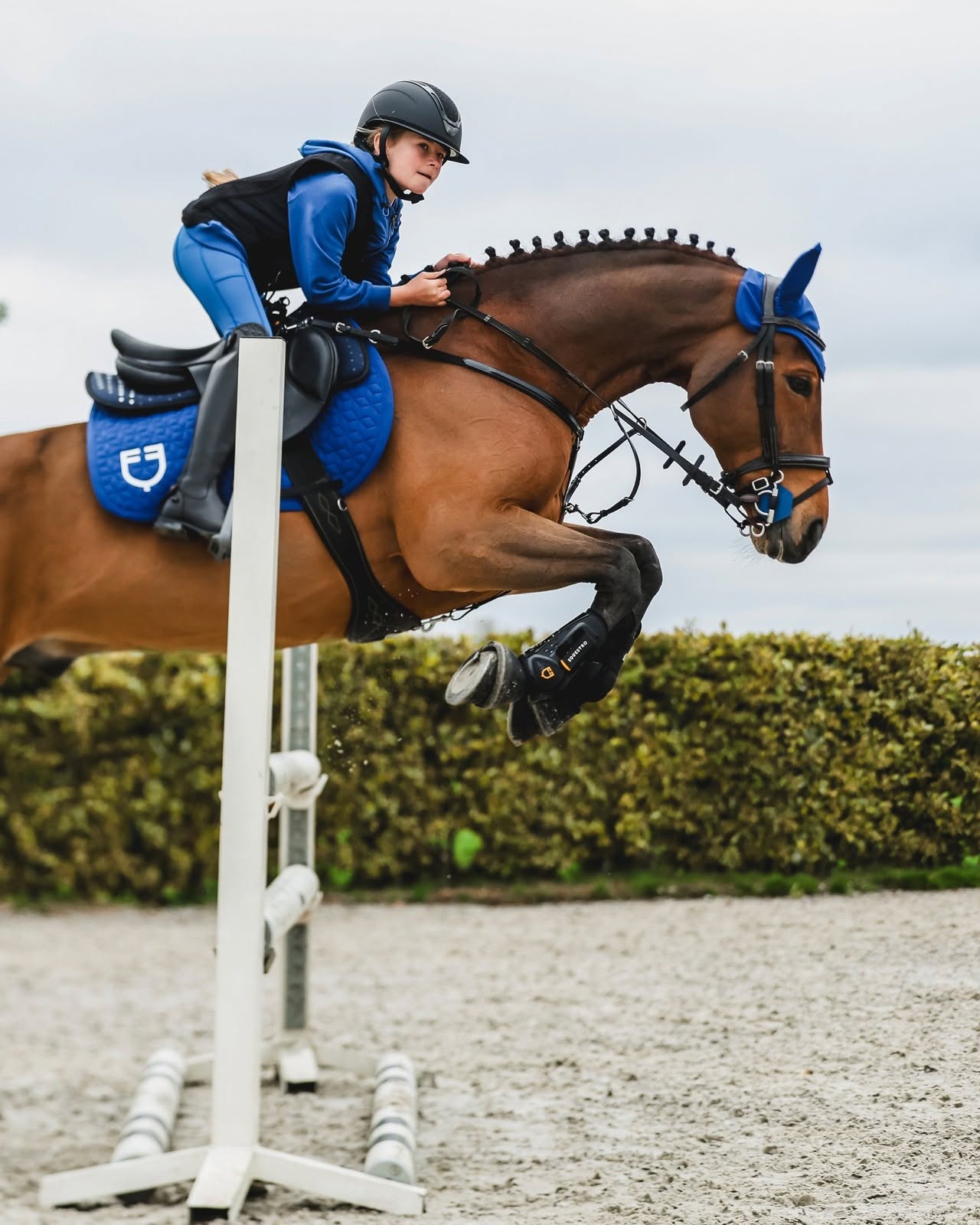 Junge Springreiterin mit Equestro-Helm über dem Sprung