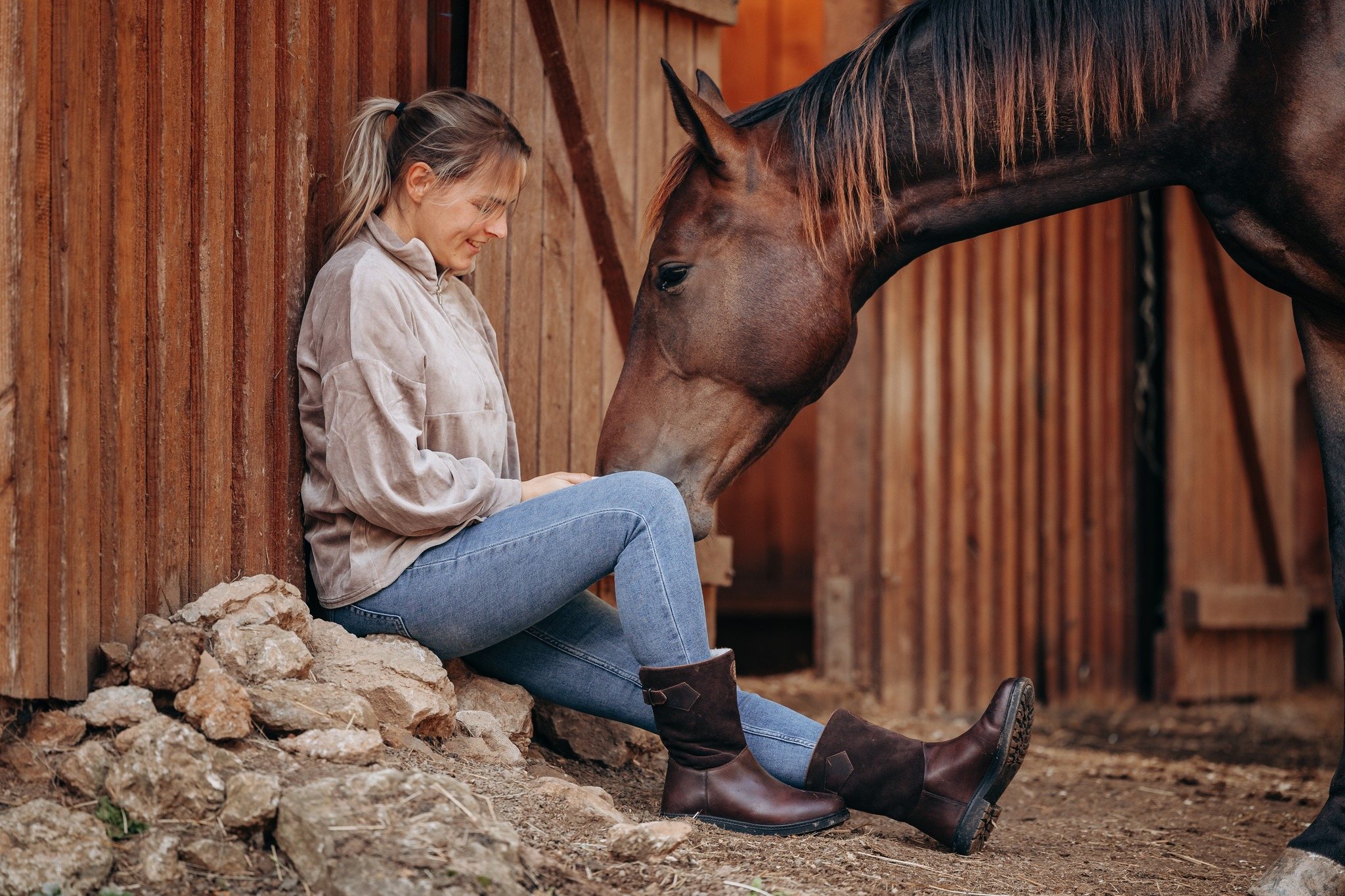 Reiterin mit Stiefeletten sitzt bei ihrem Pferd im Stall